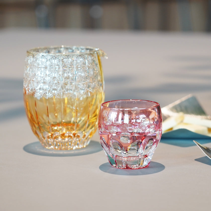 Pink cherry blossom Edo Kiriko sake cup with amber glass carafe on a table | Kagami Crystal, Satoshi Nabetani, Japan